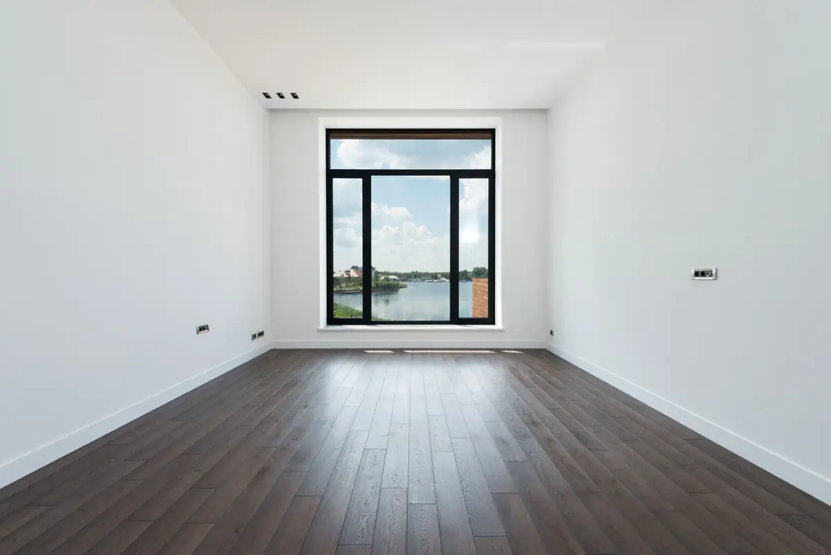 Lege lichte kamer met donkere houten plankvloer en groot raam